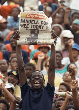 A man celebrates with a newspaper announcing Mandela goes free today.