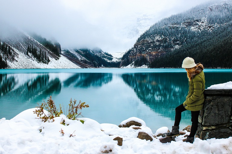 Visitor beside a turquoise mountain lake with snow along its shore in Alberta
