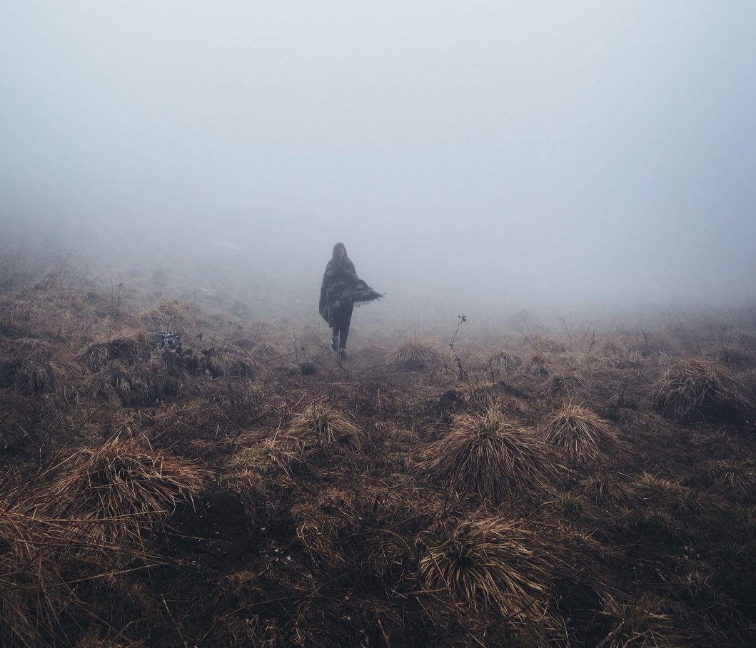 A lone traveller walking into mist across open grassland