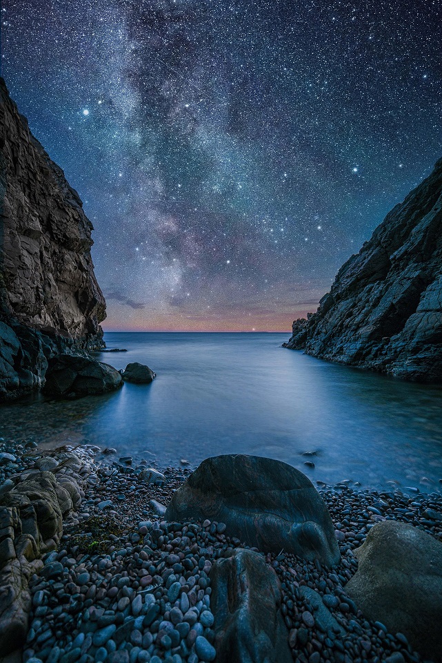 Star-filled night sky above a rocky coastal inlet in Sweden
