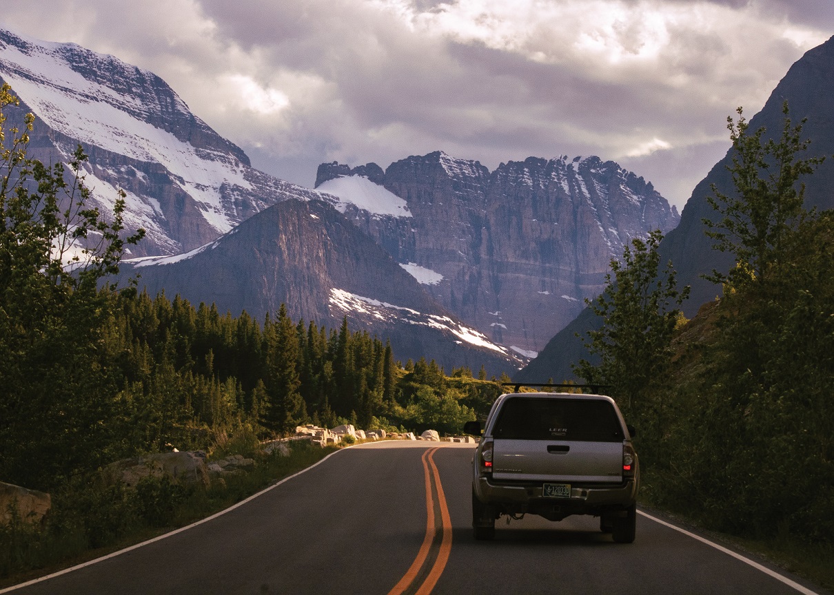 A vehicle on a winding road beneath snow-streaked mountains