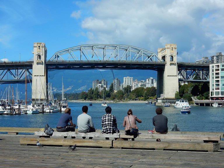 People sitting beside Vancouver’s waterfront beneath a bridge