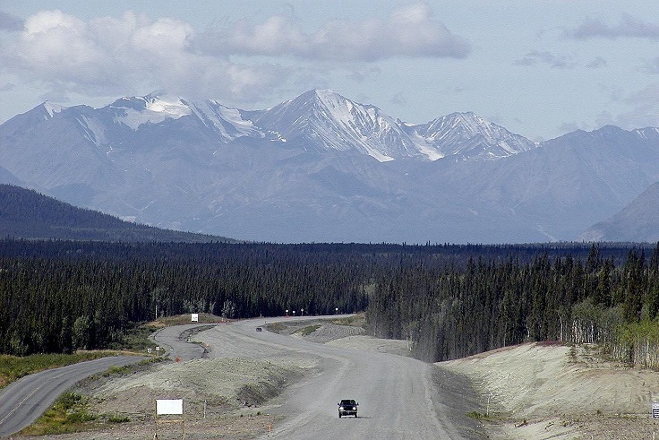 A vehicle on an open road beneath distant mountains in Yukon