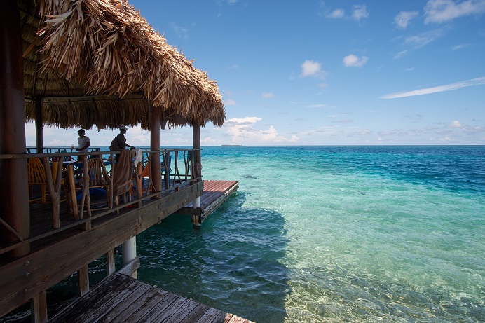 Thatched waterfront deck beside clear turquoise water in Belize