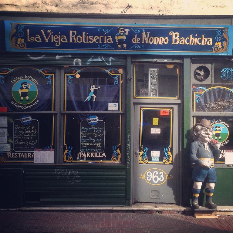 Colourful Buenos Aires rotisserie storefront with painted signs and a figure by the door