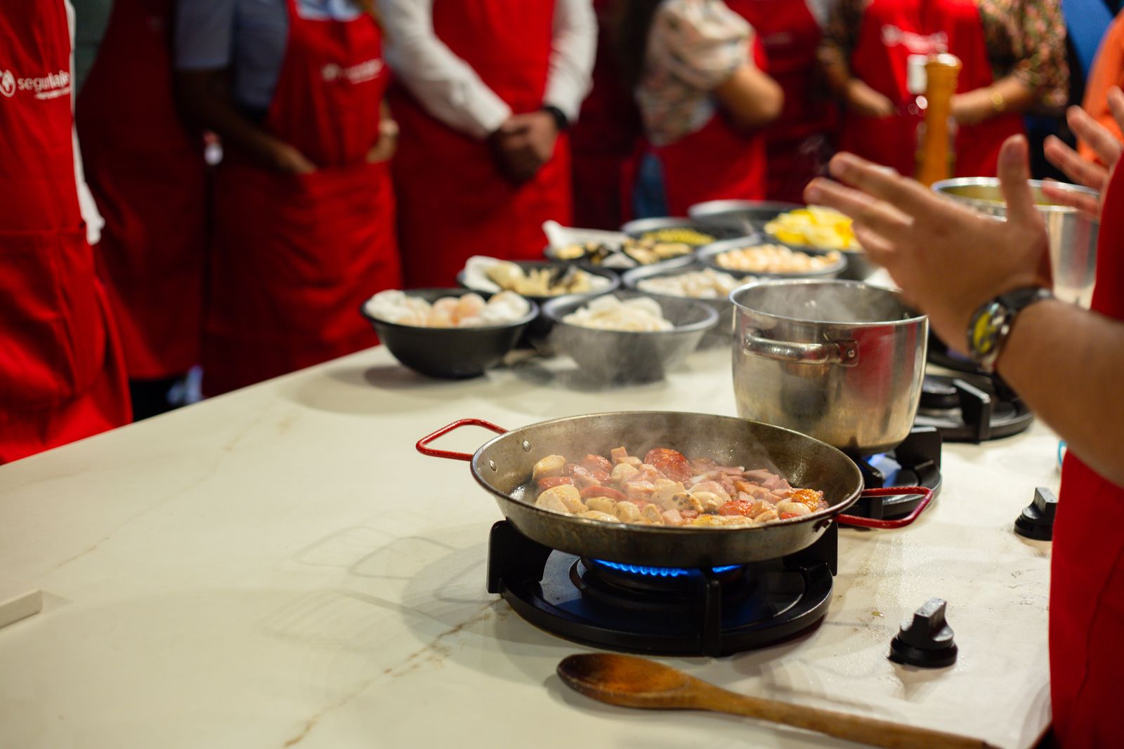 Cooking-class participants in red aprons gathered around a steaming pan