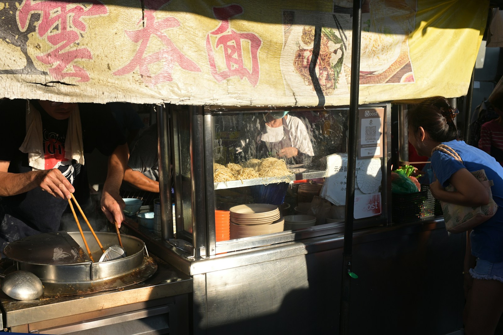 A cook preparing noodles at a street-food stall while customers wait