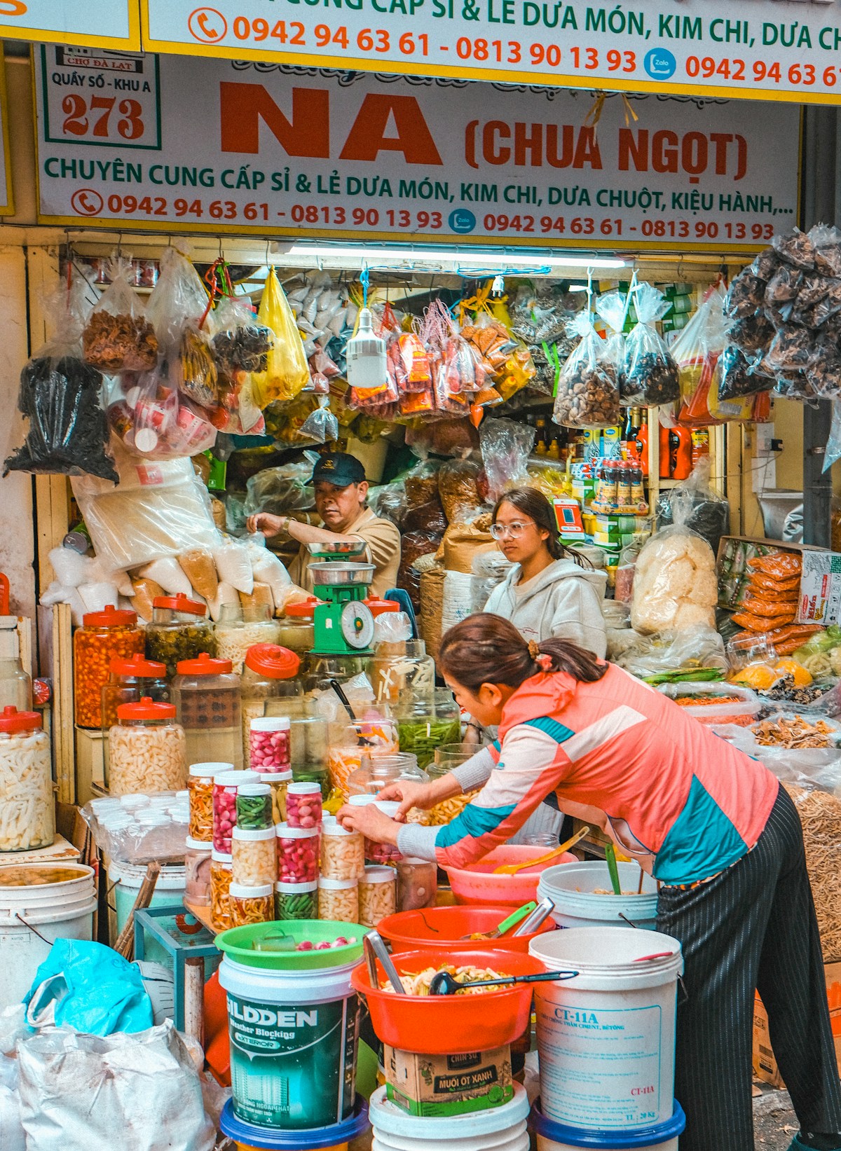 Market vendors surrounded by jars, bags and tubs of food ingredients