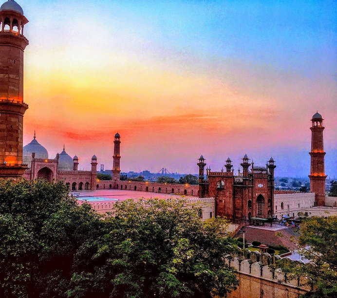 Mosque domes, minarets and red sandstone architecture beneath a colourful sunset in Lahore