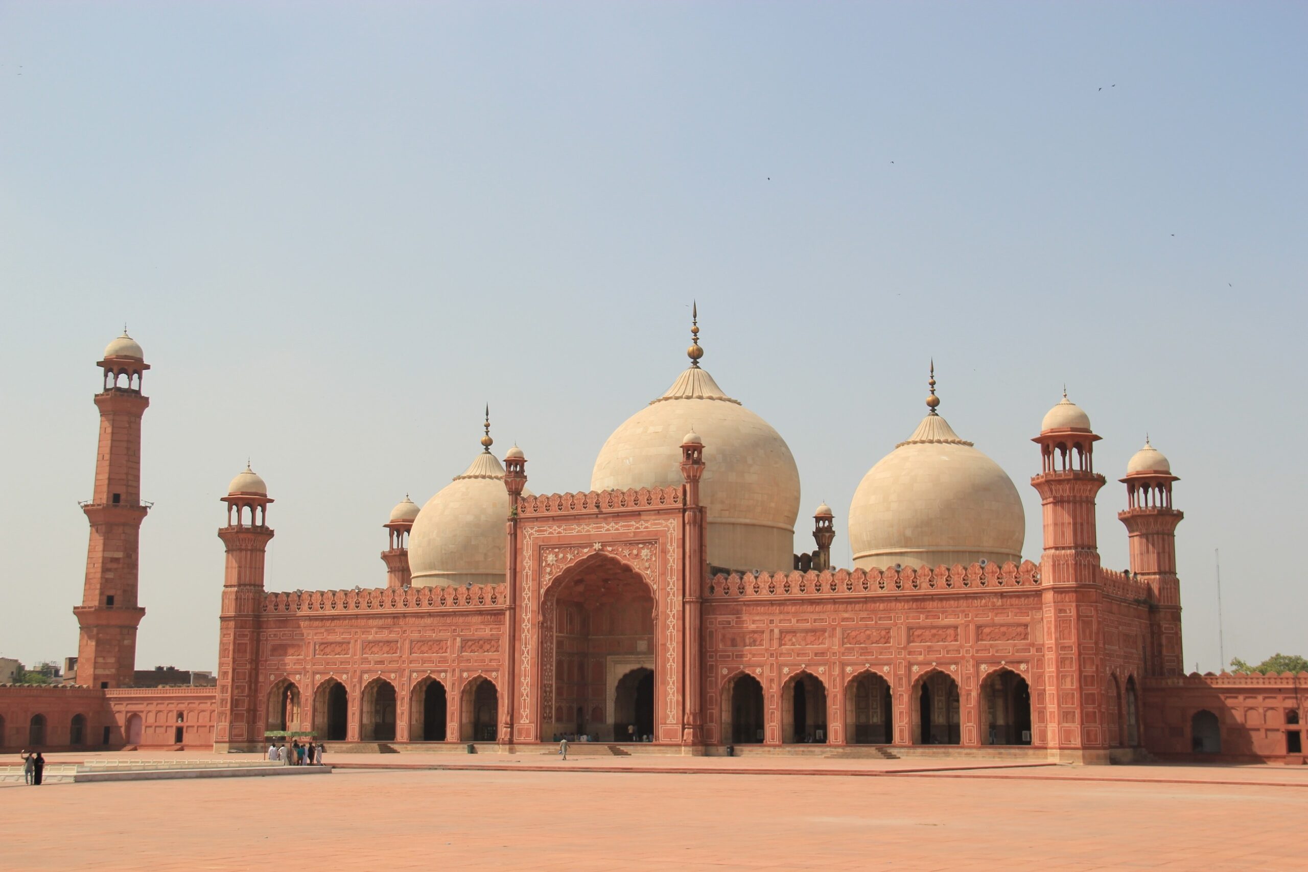 Red sandstone facade and pale domes of Badshahi Mosque in Lahore beneath a blue sky