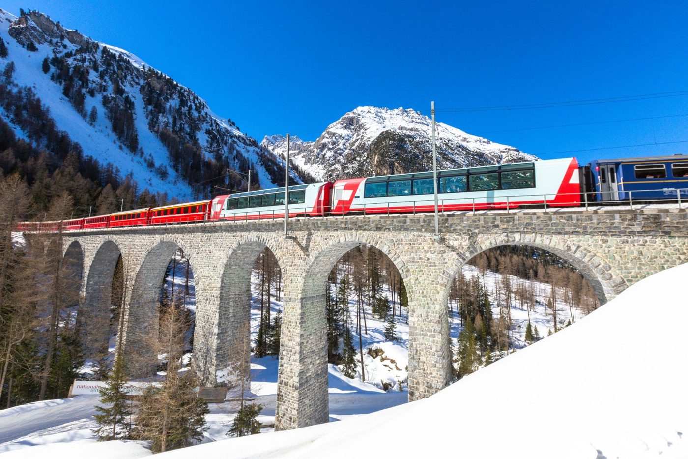 Panoramic train crossing a stone viaduct in snowy Alpine scenery