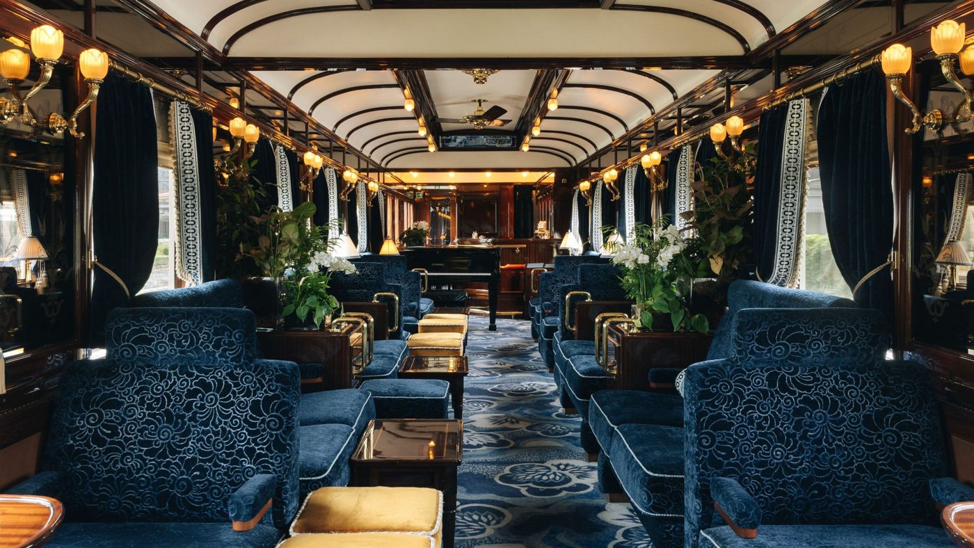 Ornate train lounge with blue upholstered chairs, lamps and wood paneling