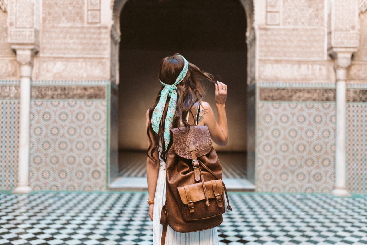 Woman with a leather backpack looking at ornate tiled architecture in Marrakesh