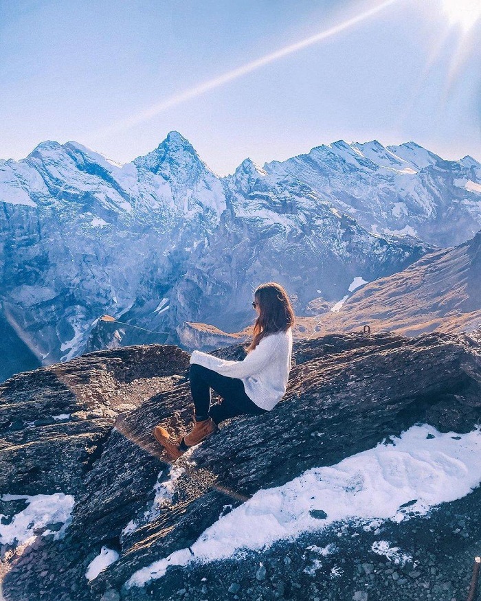 Woman sitting on a rocky slope overlooking snow-covered mountains
